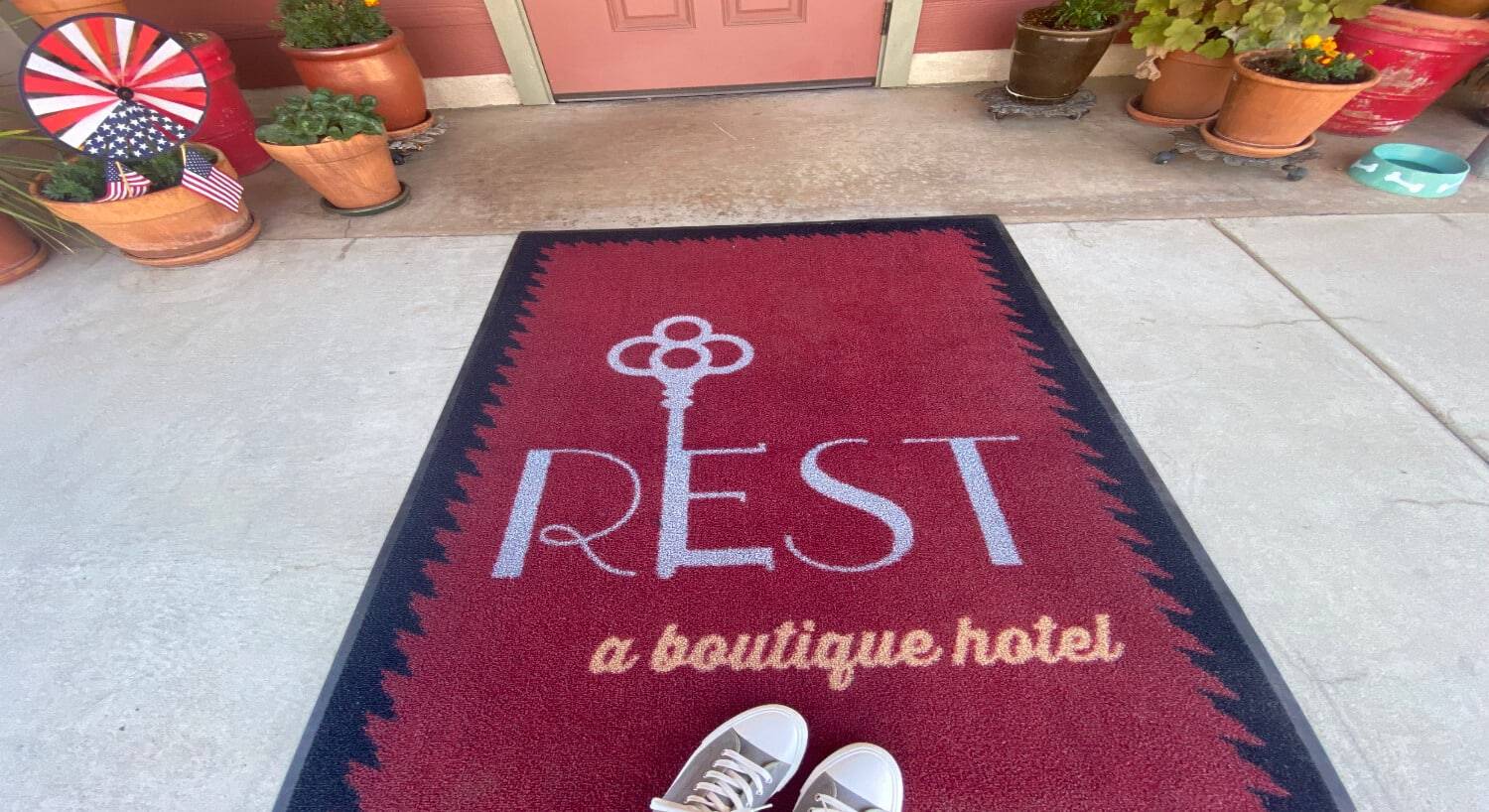 a red carpet that says Rest a boutique hotel with a key in the E and a tennis shoes at the bottom, with part of a door and flower pots on either side