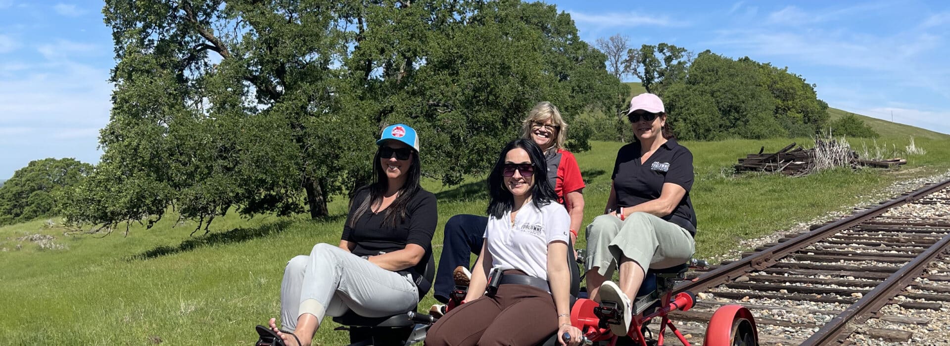 four people on a red railbike with towering oak tree and blue skies in the background