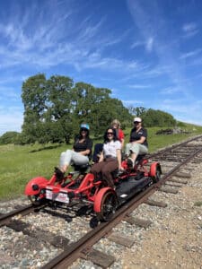 four people on a red railbike with towering oak tree and blue skies in the background