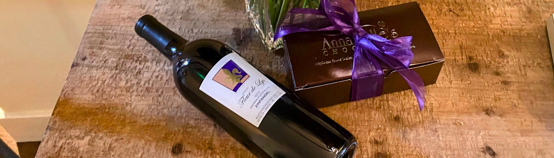 a box of chocolates with a purple ribbon and a bottle of wine