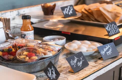 a table with breakfast foods including to go cups of fresh fruit, hard boiled eggs, and pastries