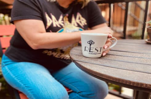 a woman at a wood table having with a coffee cup that says REST a boutique hotel with a key over the E