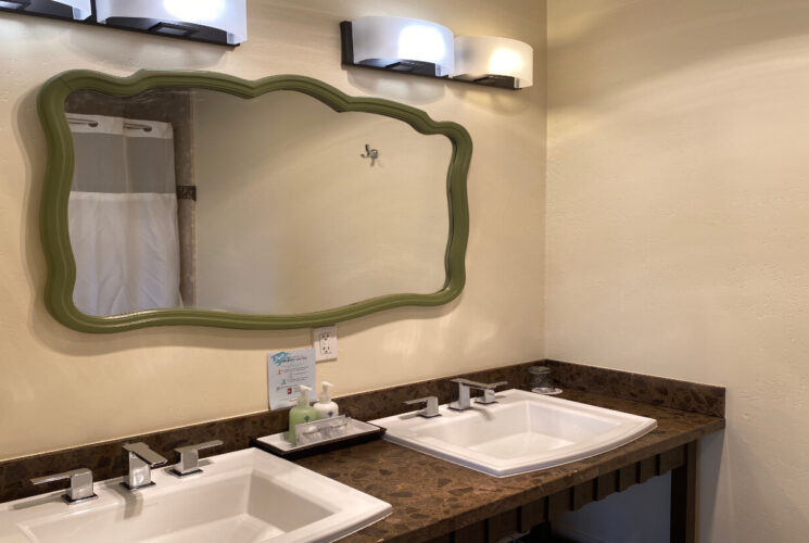 a bathroom with double sinks, bath amenities on the counter, a large rectangular mirror and light fixtures above the mirror.