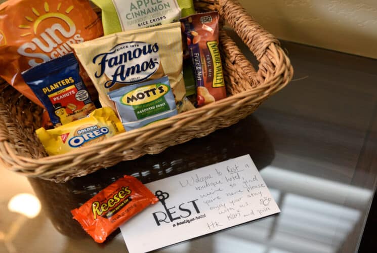 a basket of snacks on a small table with a note on a notecard that says REST a boutique hotel.