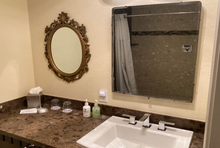 a bathroom with a laminate countertop, a white rectangular sink, bath amenities on the counter, and 2 mirrors above the sink and counter.