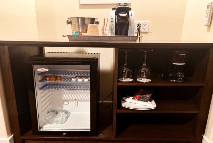 a built in buffet table with a coffeemaker and ice bucket on top, a mini fridge underneath on one side, and wine glasses, and amenities on the other side.