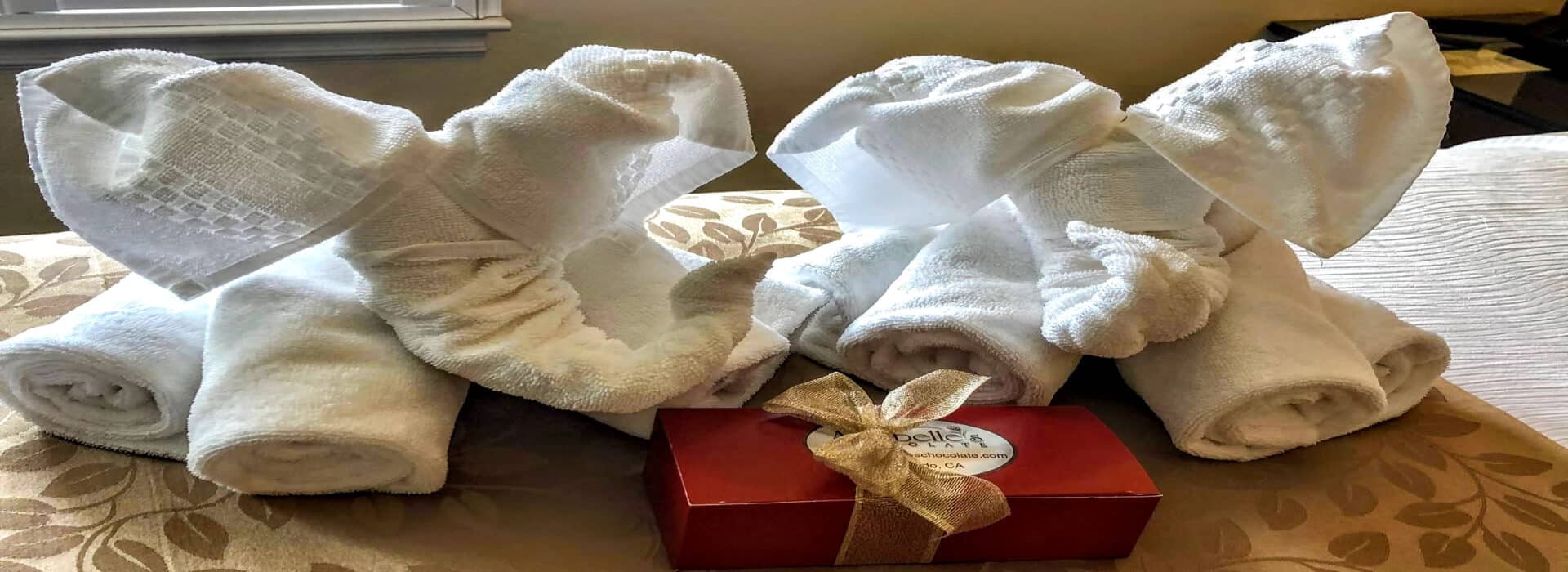 two towel art elephants on a bed with a red box of chocolates