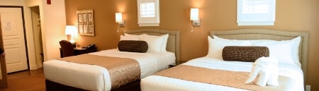 A bedroom with 2 queen beds with wall lamps in between and on the sides of the bed.
