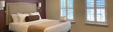 A bedroom with burgundy and tan walls, a queen bed with an elephant towel art on the bed, and a window on the outside wall