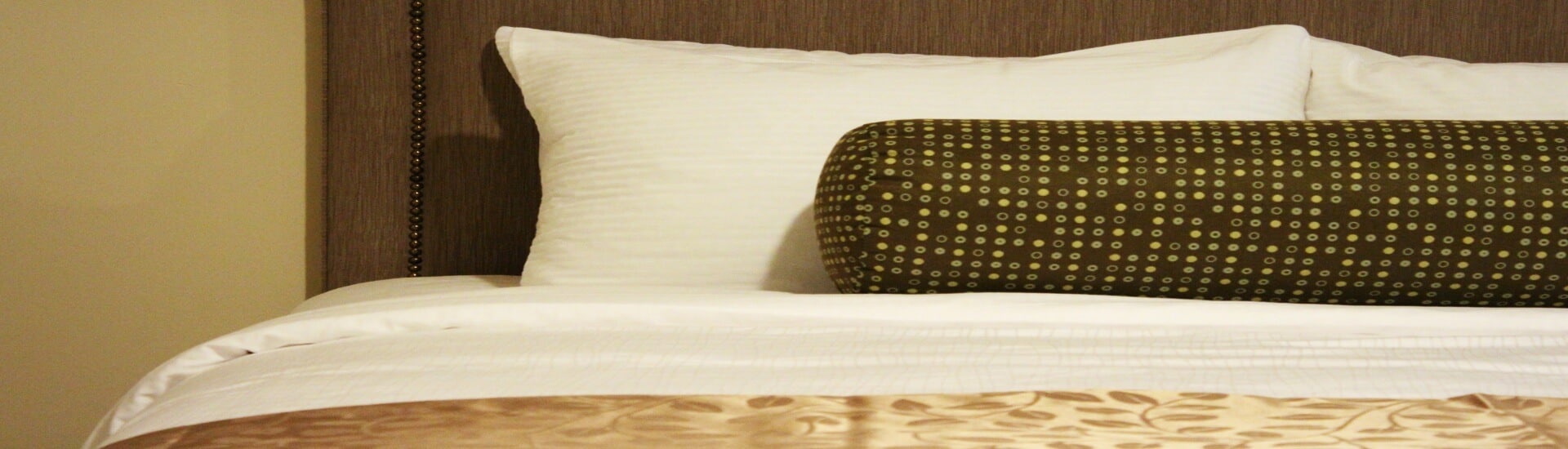 a bed with white and gold bedding, and a round brown pillow
