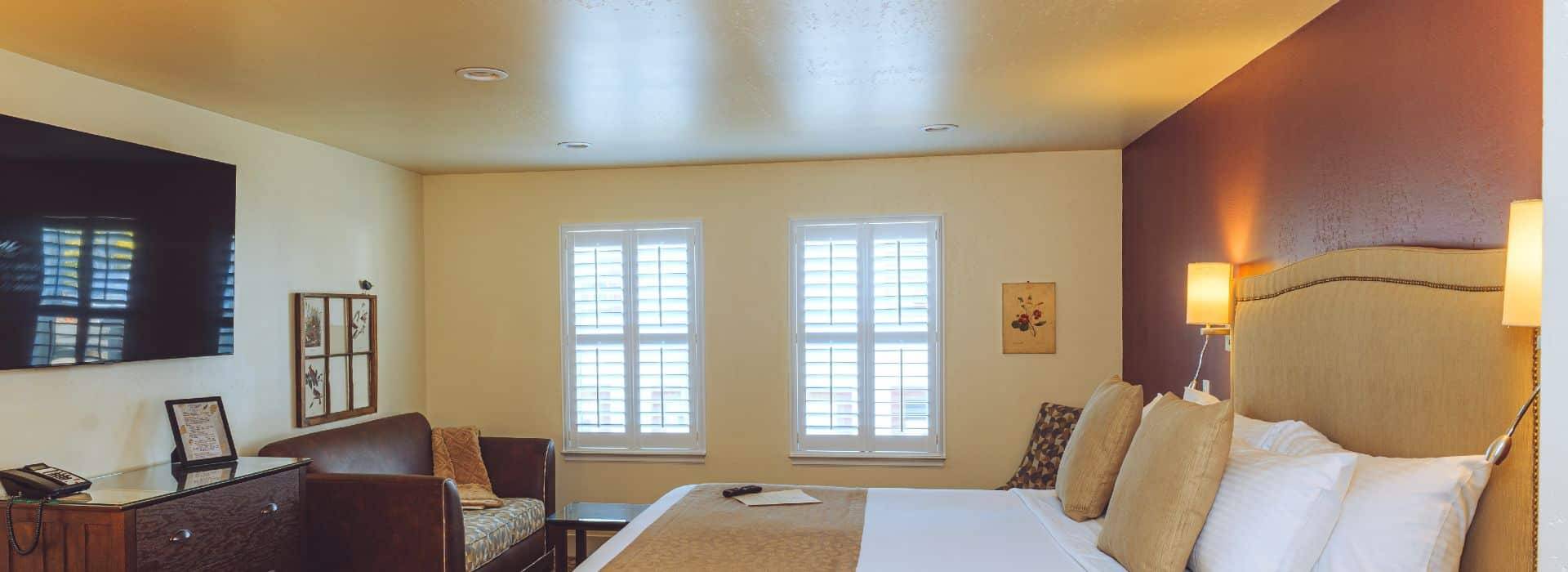 guest room view of bed, dresser and couch in background.  Color tones of white and brown