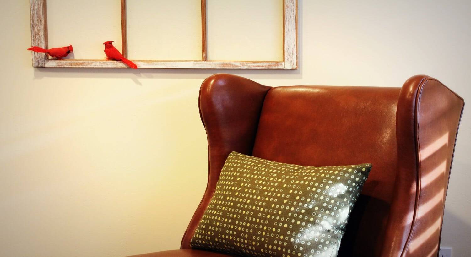 a red wingback leather chair with a gold and tan pillow on the chair.
