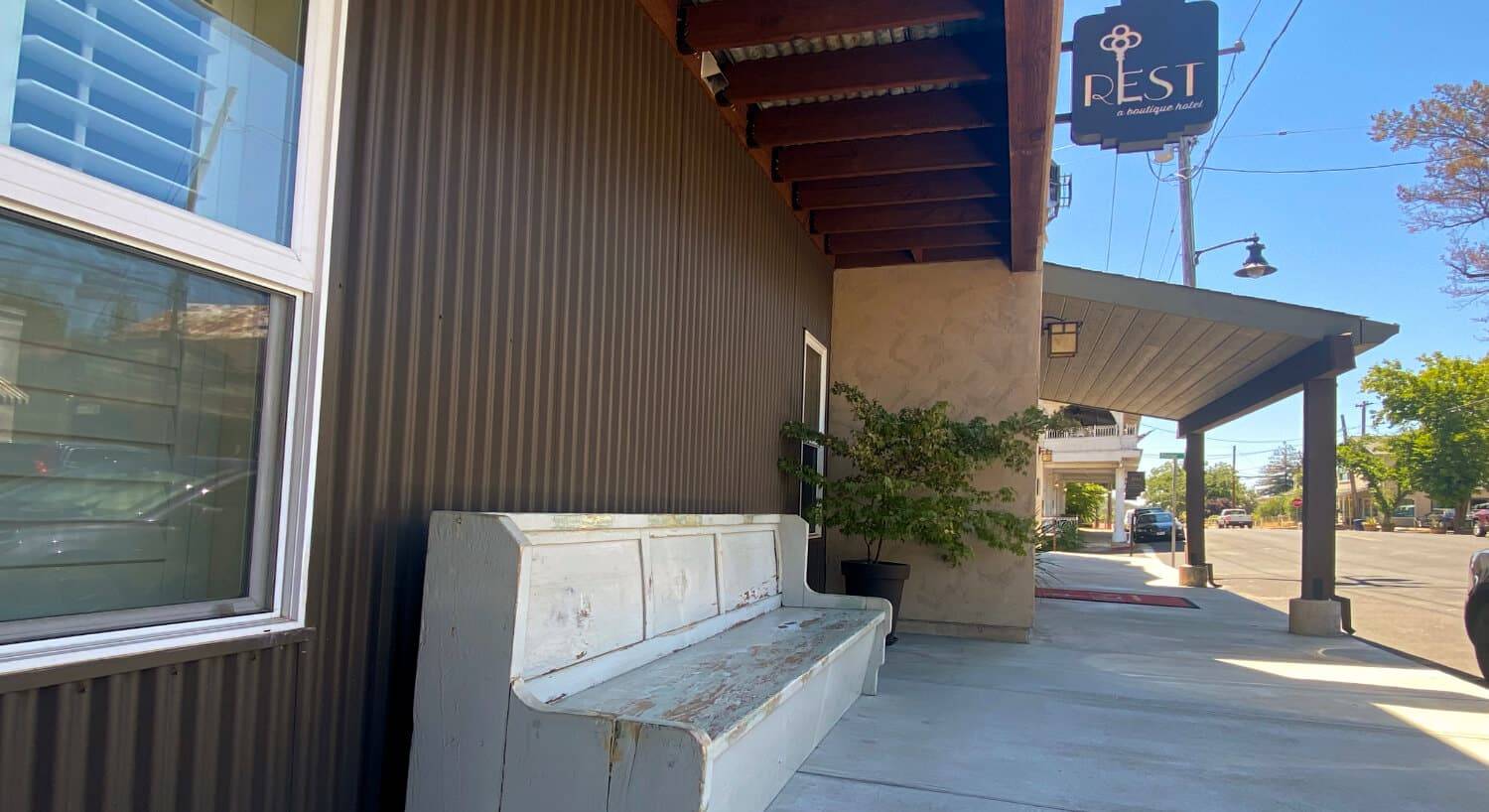 a brown sided building and a stone bench in front, with the sign Rest a boutique hotel hanging over an awning.