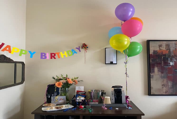 a table set up with party food, a bunch of colorful balloons nearby and a sign that say Happy Birthday