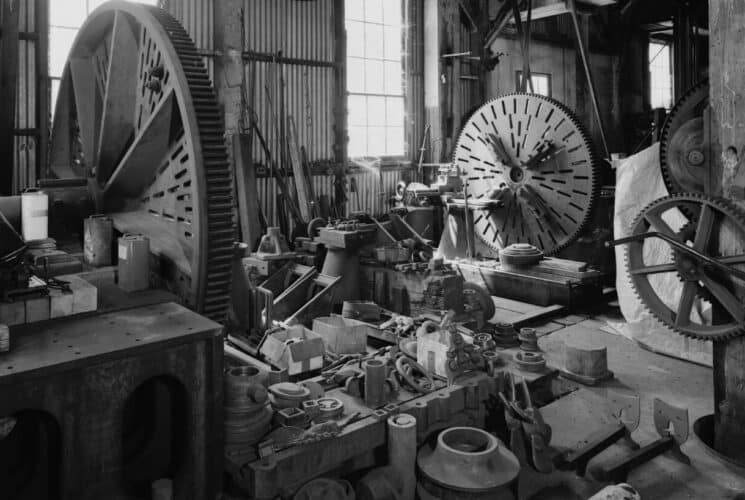 a black and white photo of a barn with old fashioned equipment and a large cog wheels inside