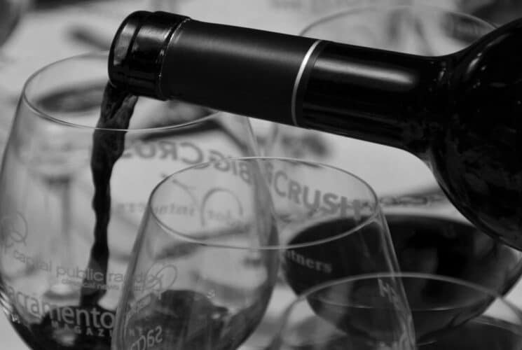a black and white photo of a bottle of wine being poured into a wine glass